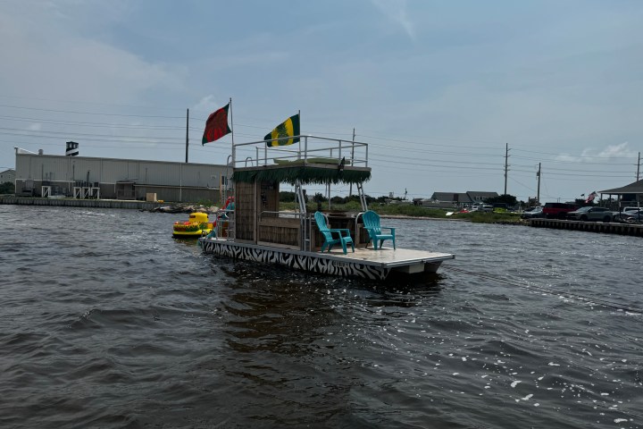 Small floating deck with chairs and flags on a river near an industrial area.