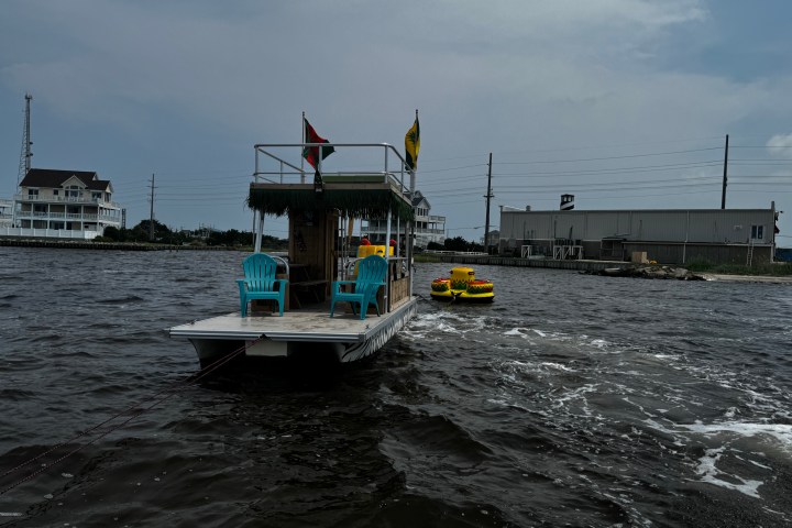 Boat with chairs on water towing a yellow raft, under cloudy sky.